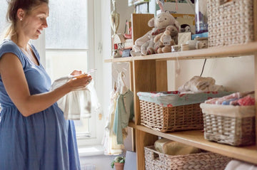 A pregnant woman in a nursery sorting out baby clothes.